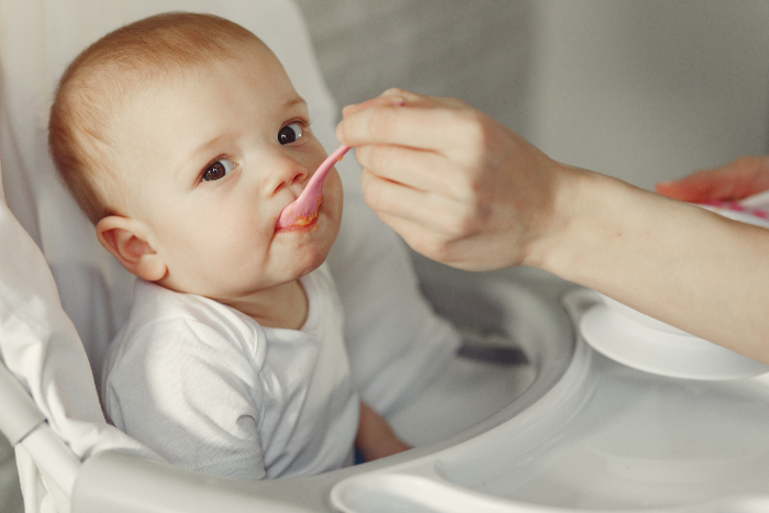 mother feeding her little baby in a kitchen - Como deve ser a alimentação do seu bebê no primeiro ano de vida